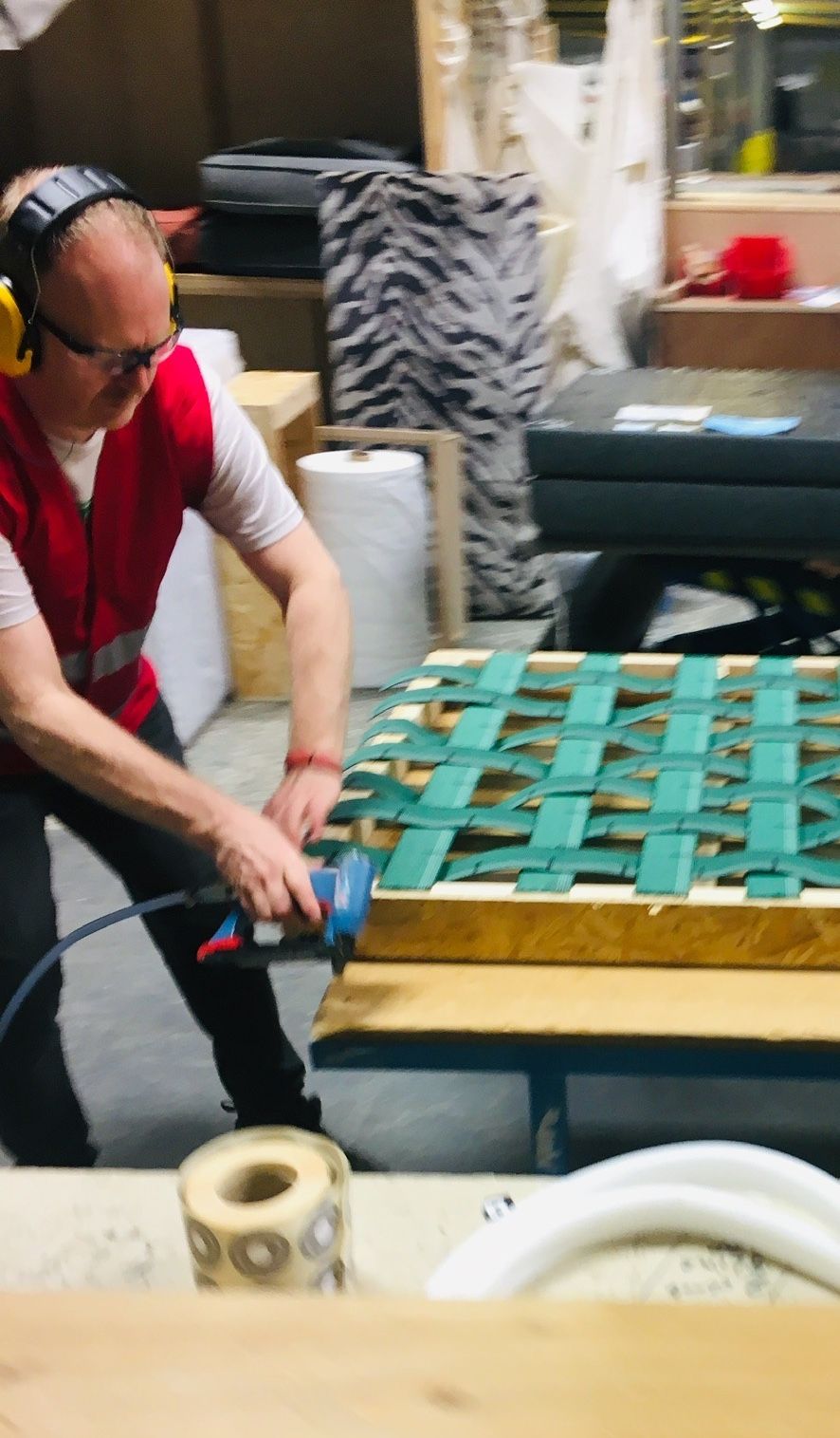 A worker stapling webbing to a sofa frame during assembly